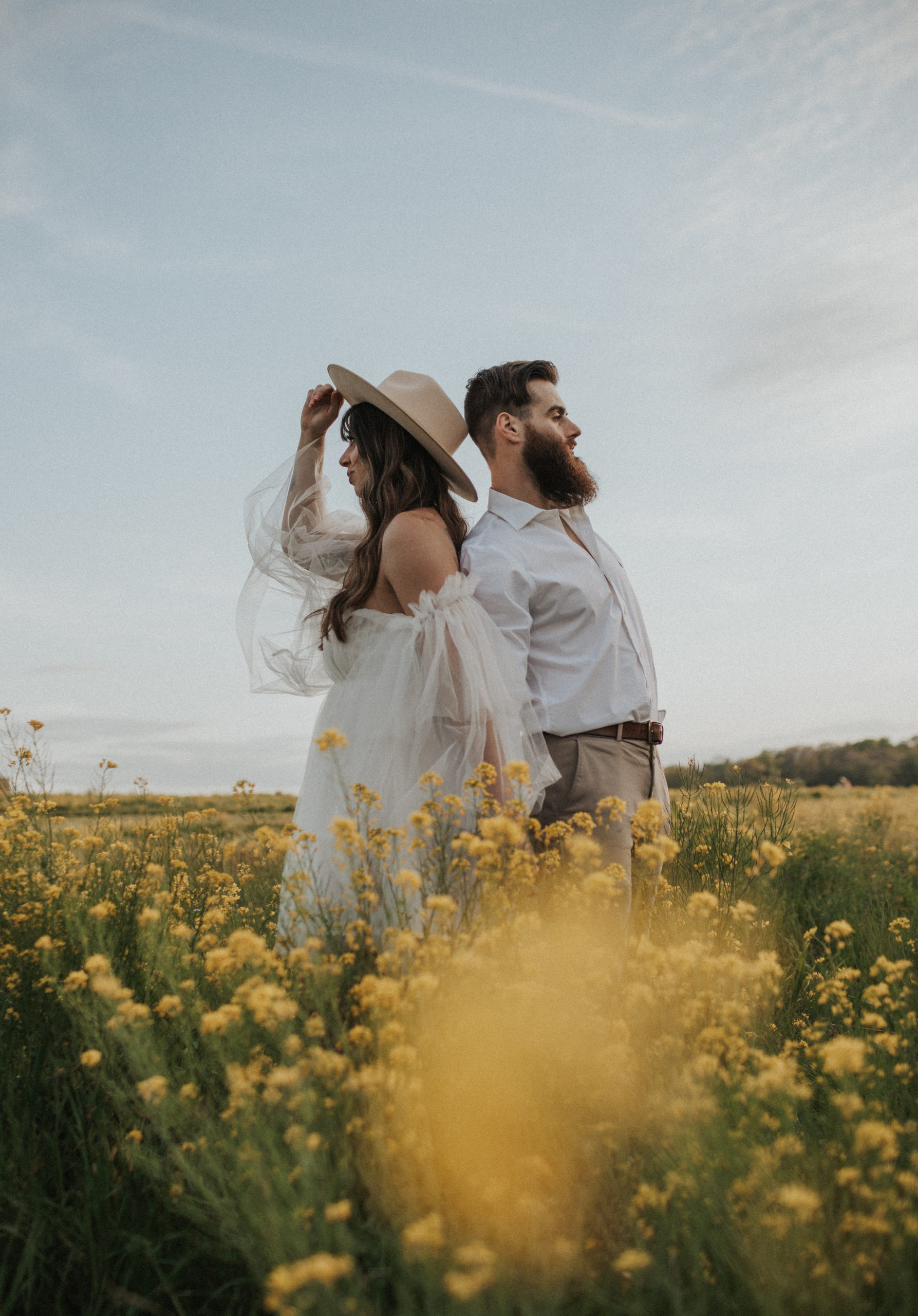 Couple standing back to back in a yellow flower field looking in opposite directions