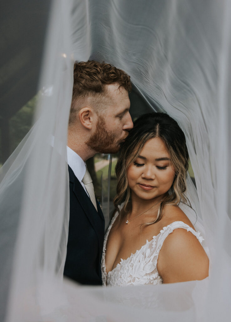 Bride and Groom posing for wedding photography under veil 