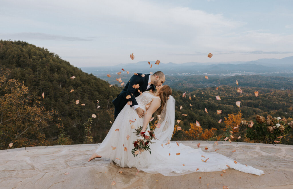 Bride and Groom kissing under pedals with mountain backdrop