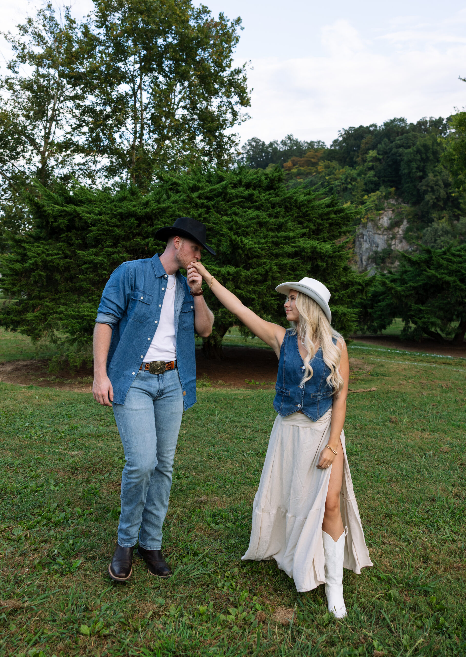 Engagement photo of a couple walking through a countryside path on an overcast day, captured in a modern Western style with neutral tones and minimal, editorial-inspired outfits.