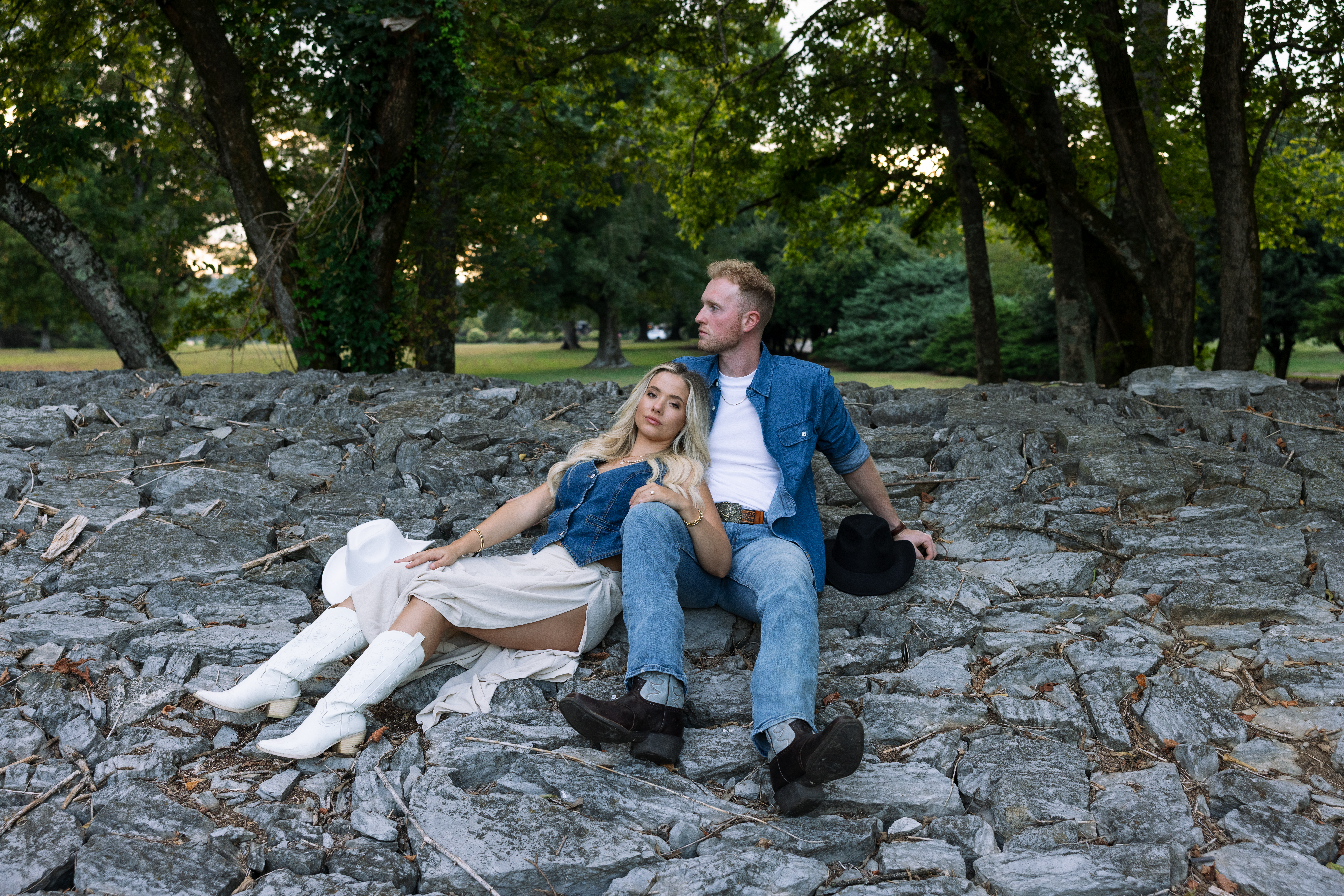 Modern Western engagement session featuring a stylish couple sitting on a stone bridge, wearing cowboy boots and denim, captured with natural golden sunlight.