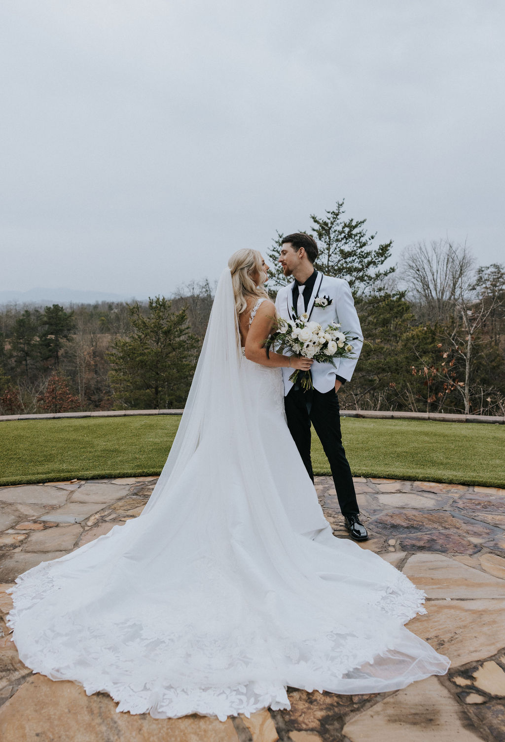 The bride and groom gaze at each other lovingly while standing on a stone terrace, surrounded by natural mountain scenery at Nichols Heir Glass House, captured by a Knoxville wedding photographer