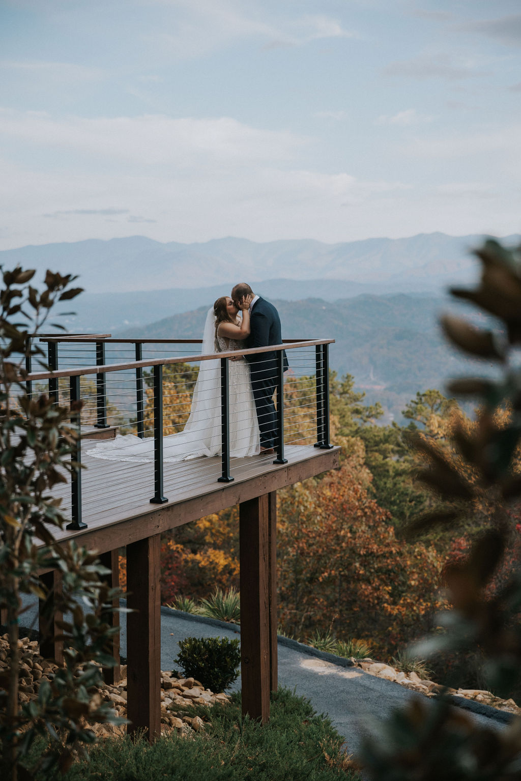 Romantic kiss on a mountaintop balcony, with the couple surrounded by colorful fall trees and panoramic Smoky Mountain views; photographed at a Mountain View Venue in the Smoky Mountains