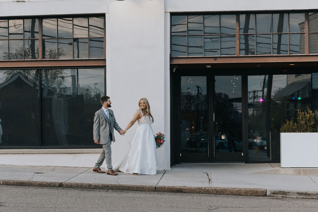 Bride and groom holding hands and smiling while walking outside The Press Room Knoxville, captured during a wedding by a Knoxville wedding photographer.