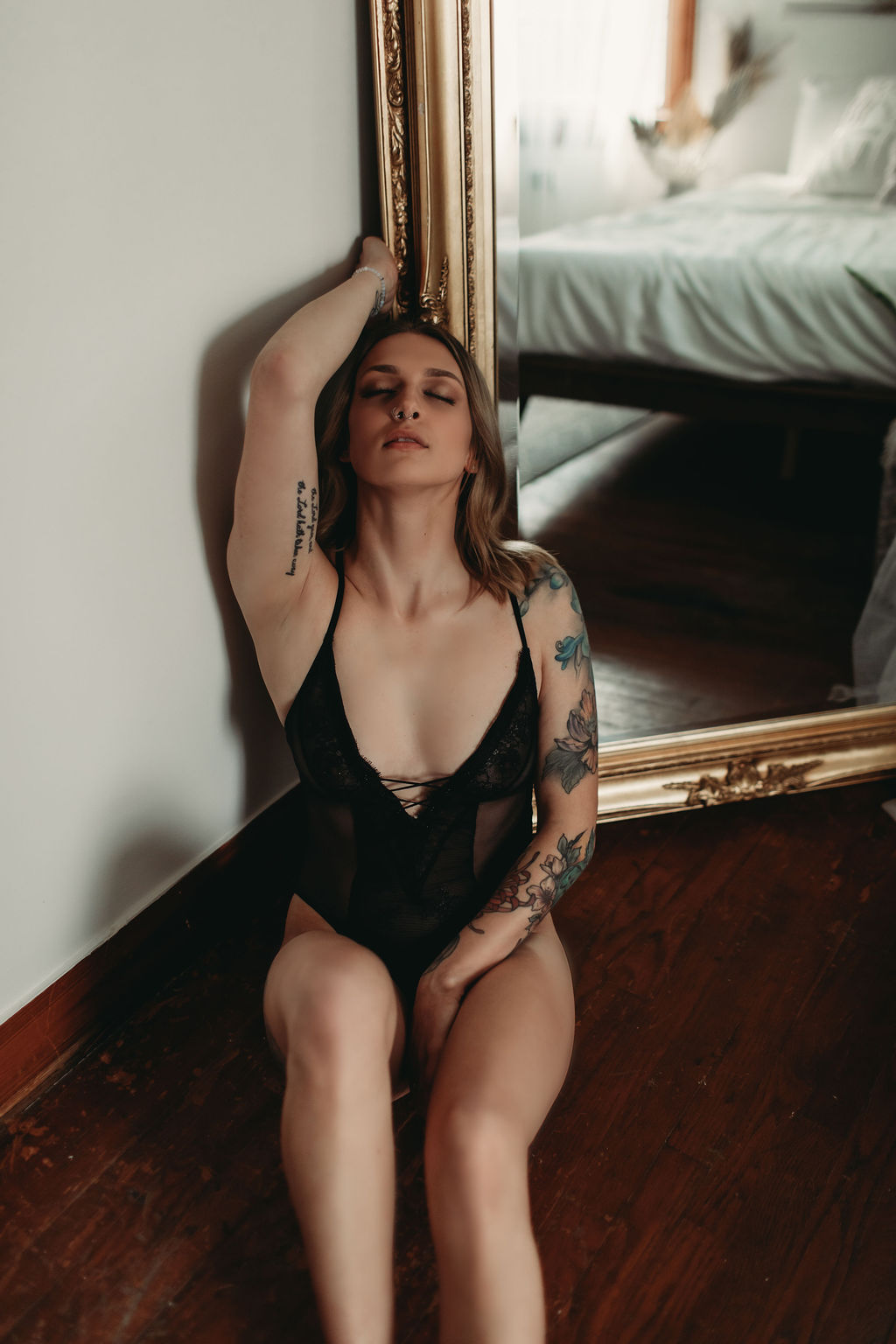 Woman in black bodysuit leaning against mirror with eyes closed during intimate boudoir photography shoot