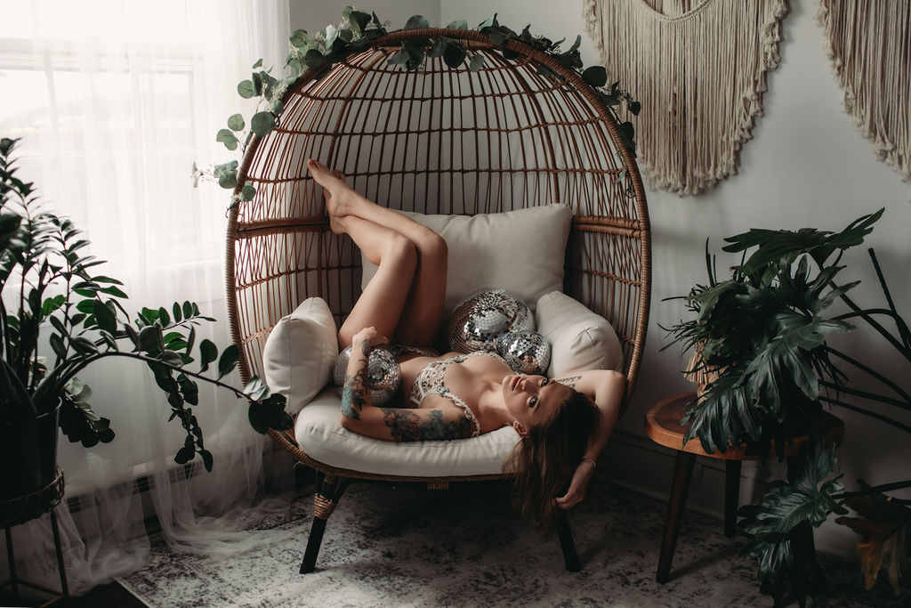 Woman laying on rattan chair with legs in the air with disco balls around her, while wearing cream set. 