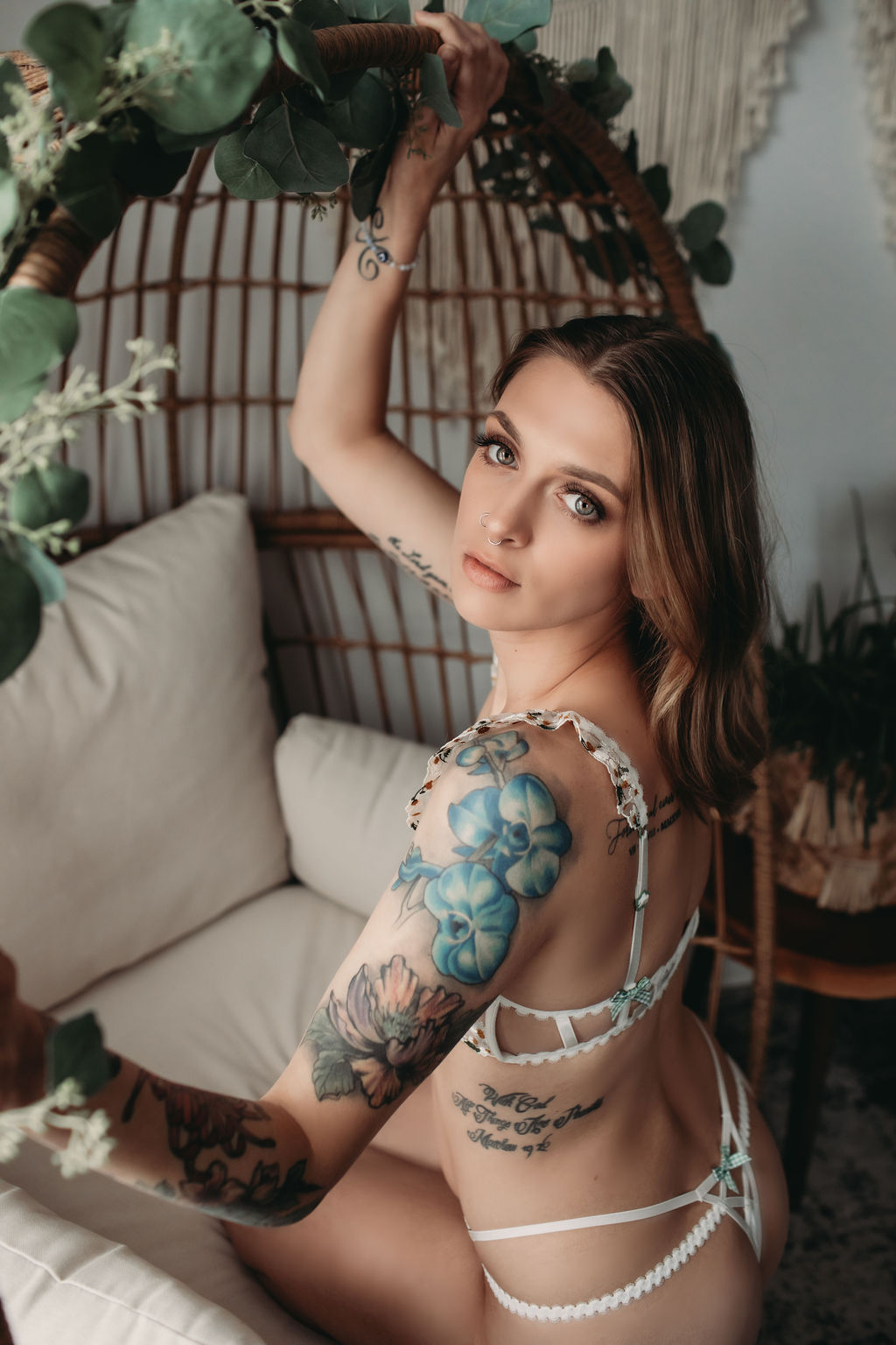 Woman in cream set sitting on big rattan chair looking over her shoulder during boudoir photography shoot. 