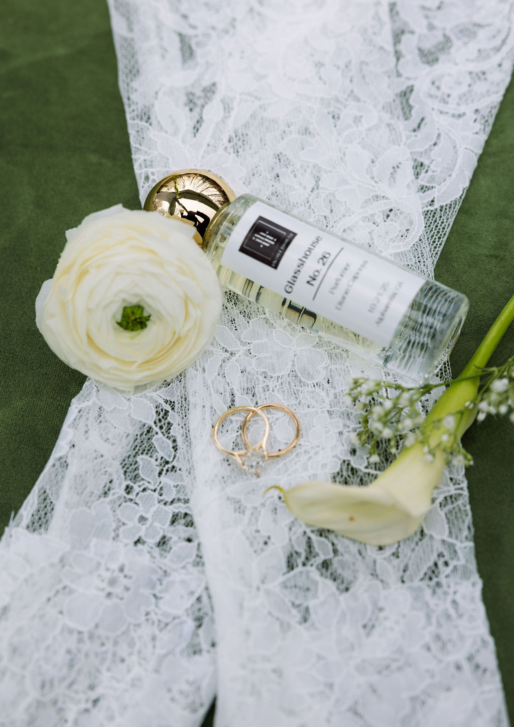 Wedding rings and perfume styled on lace with florals, detailed flat lay reflecting the intentional design choices that show what do wedding planners do in coordinating every element.