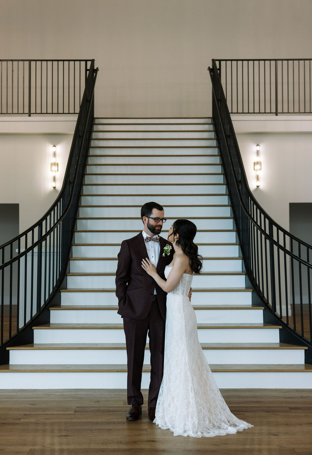 Bride and groom standing together at the base of a sweeping staircase inside Nichols Heir, elegant indoor Tennessee wedding portrait.