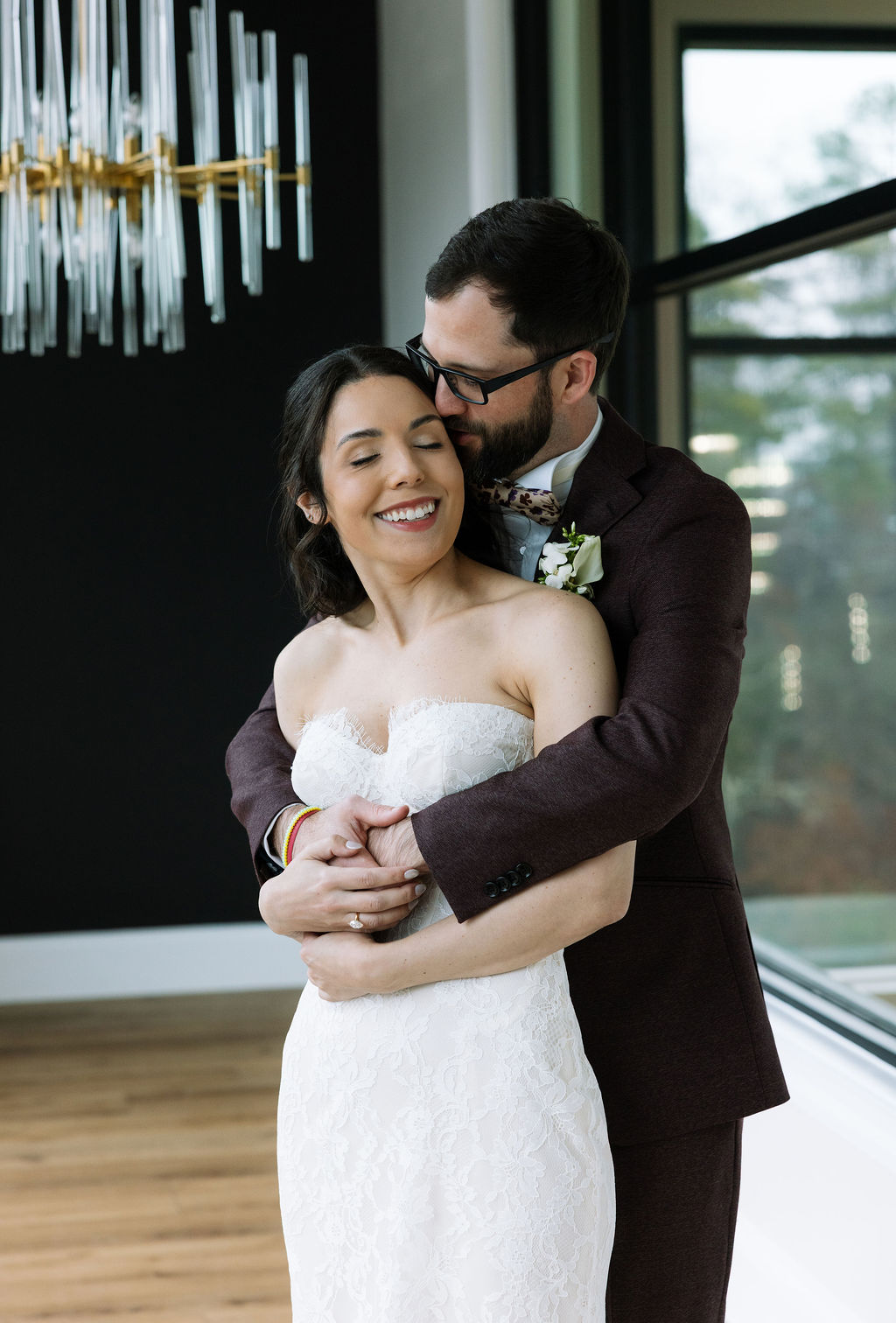 Bride smiling as groom embraces her in the Glass House at Nichols Heir, soft indoor light reflecting what do wedding planners do to create calm portrait time despite rain.