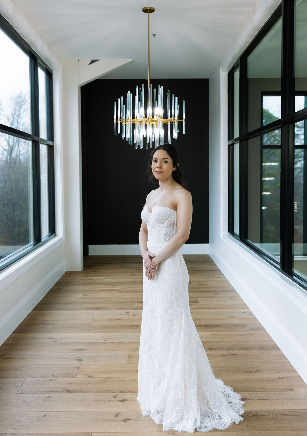 Bride standing beneath modern chandelier lighting in the Glass House at Nichols Heir, true-to-color indoor wedding portrait on a rainy Tennessee afternoon.