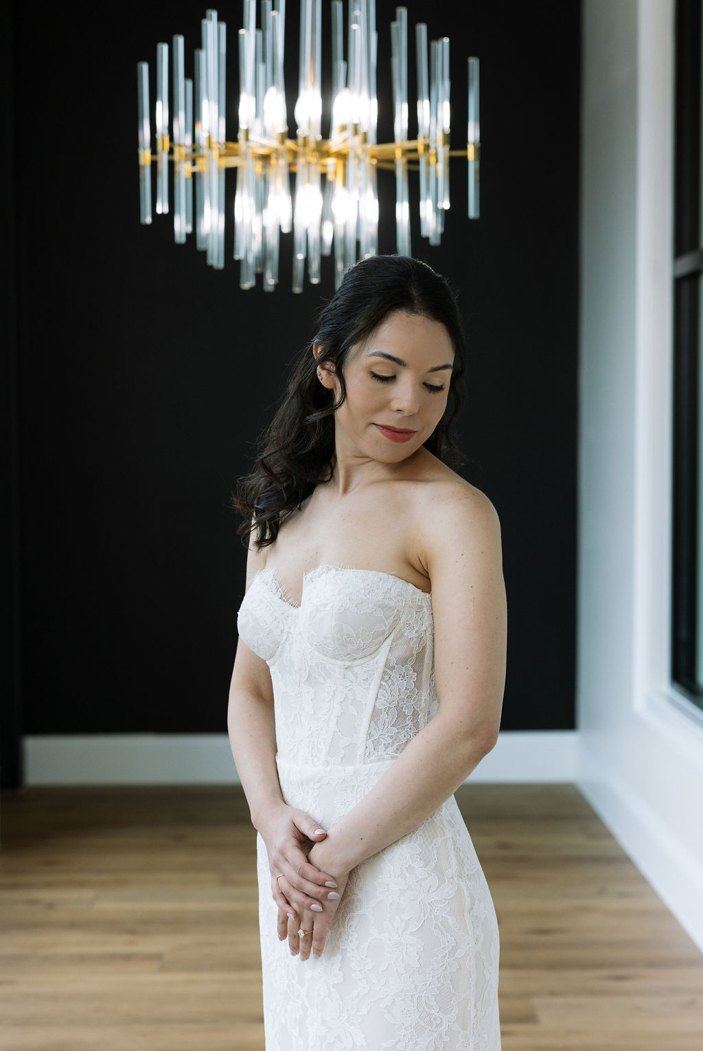 Bride standing beneath modern chandelier lighting in the Glass House at Nichols Heir, soft indoor light ideal for true-to-color wedding photography on a rainy Tennessee day.