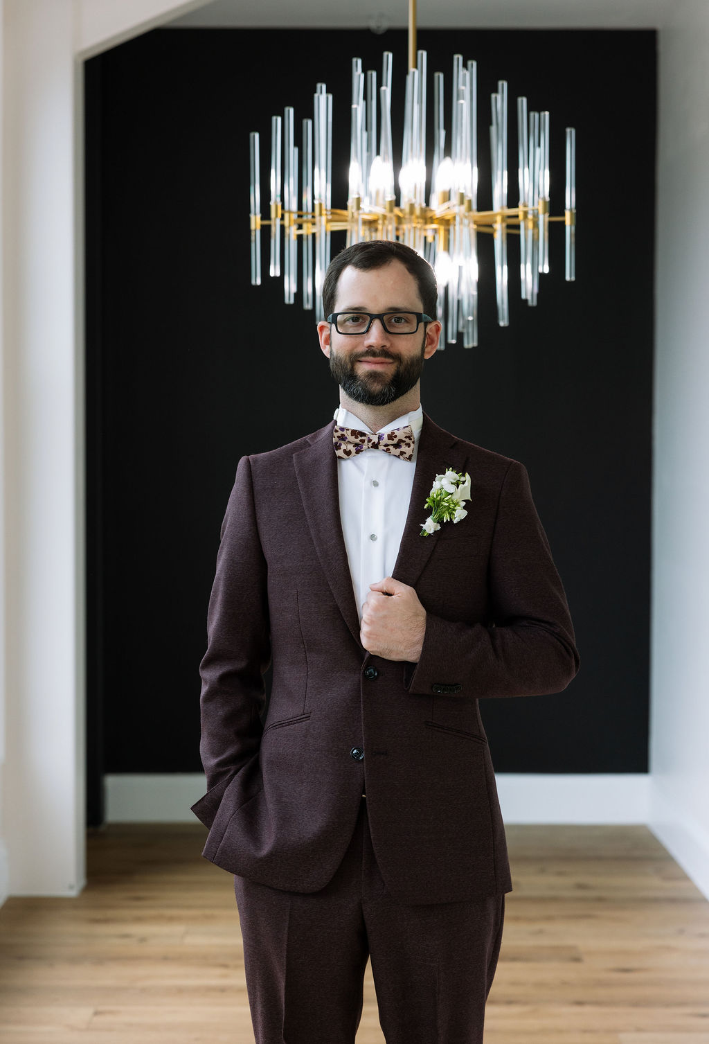 Groom standing beneath a modern chandelier in the Glass House at Nichols Heir, indoor portrait captured during a rain-adjusted Tennessee wedding day.