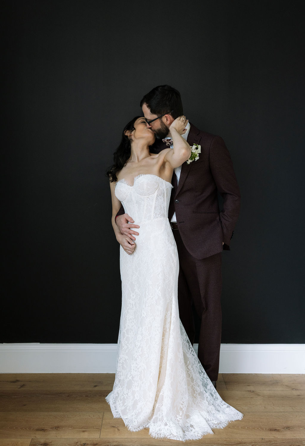 Bride and groom kissing against a dark backdrop inside Nichols Heir, a composed indoor portrait made possible by what do wedding planners do when weather shifts plans.