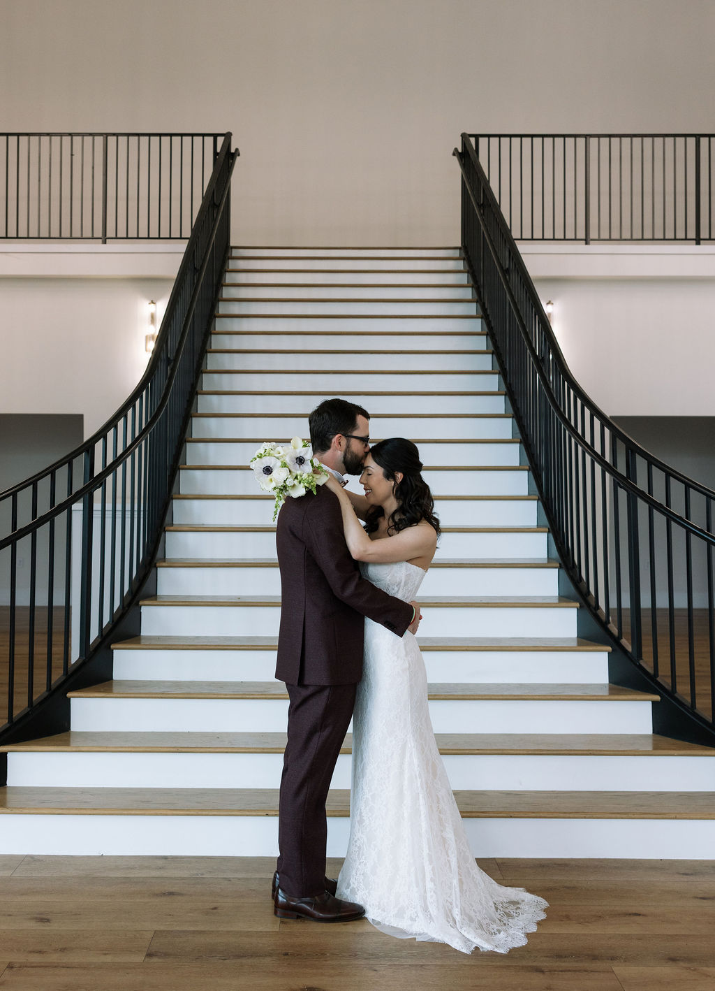 Bride and groom embracing at the base of the grand staircase inside Nichols Heir in Tennessee, elegant indoor portrait created during a rain-adjusted wedding timeline.