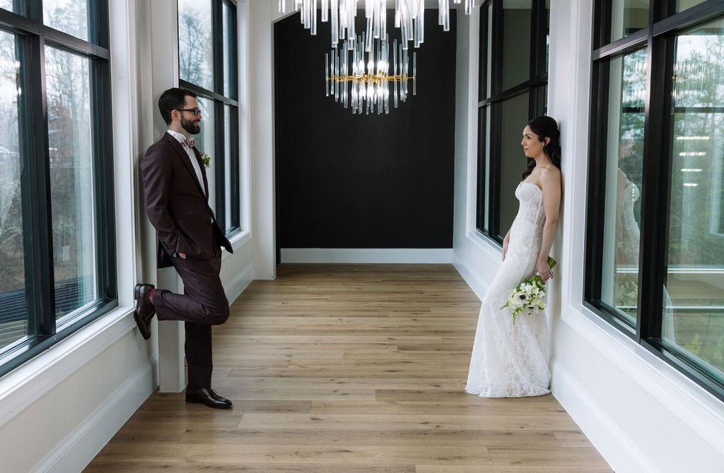 Bride and groom standing across from each other in the Glass House at Nichols Heir, soft window light creating true-to-color indoor wedding portraits on a rainy Tennessee wedding day.