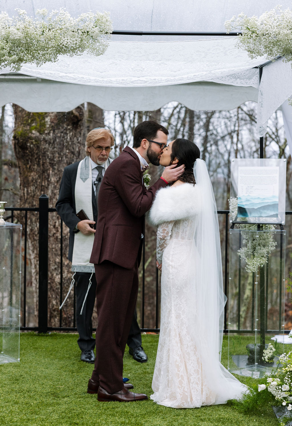 Bride and groom sharing their first kiss beneath a rain-covered ceremony tent, coordinated timeline reflecting what do wedding planners do to protect the moment.