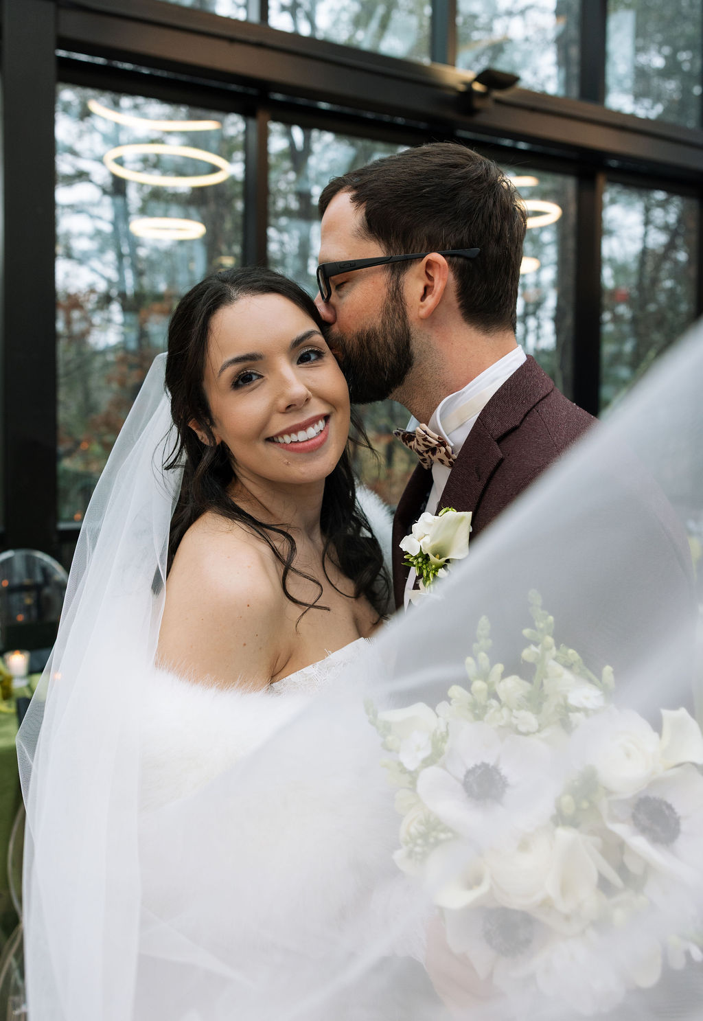 Bride smiling beneath her veil as groom kisses her temple inside Nichols Heir, intimate indoor portrait shaped by what do wedding planners do to create calm transitions on a rainy wedding day.