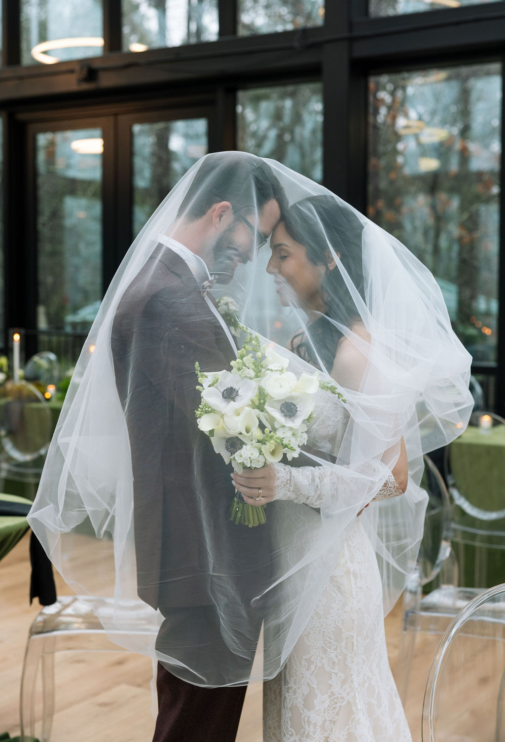 Bride and groom standing under the veil inside Nichols Heir’s Glass House, soft diffused light ideal for true-to-color wedding photography on a Tennessee rain day.