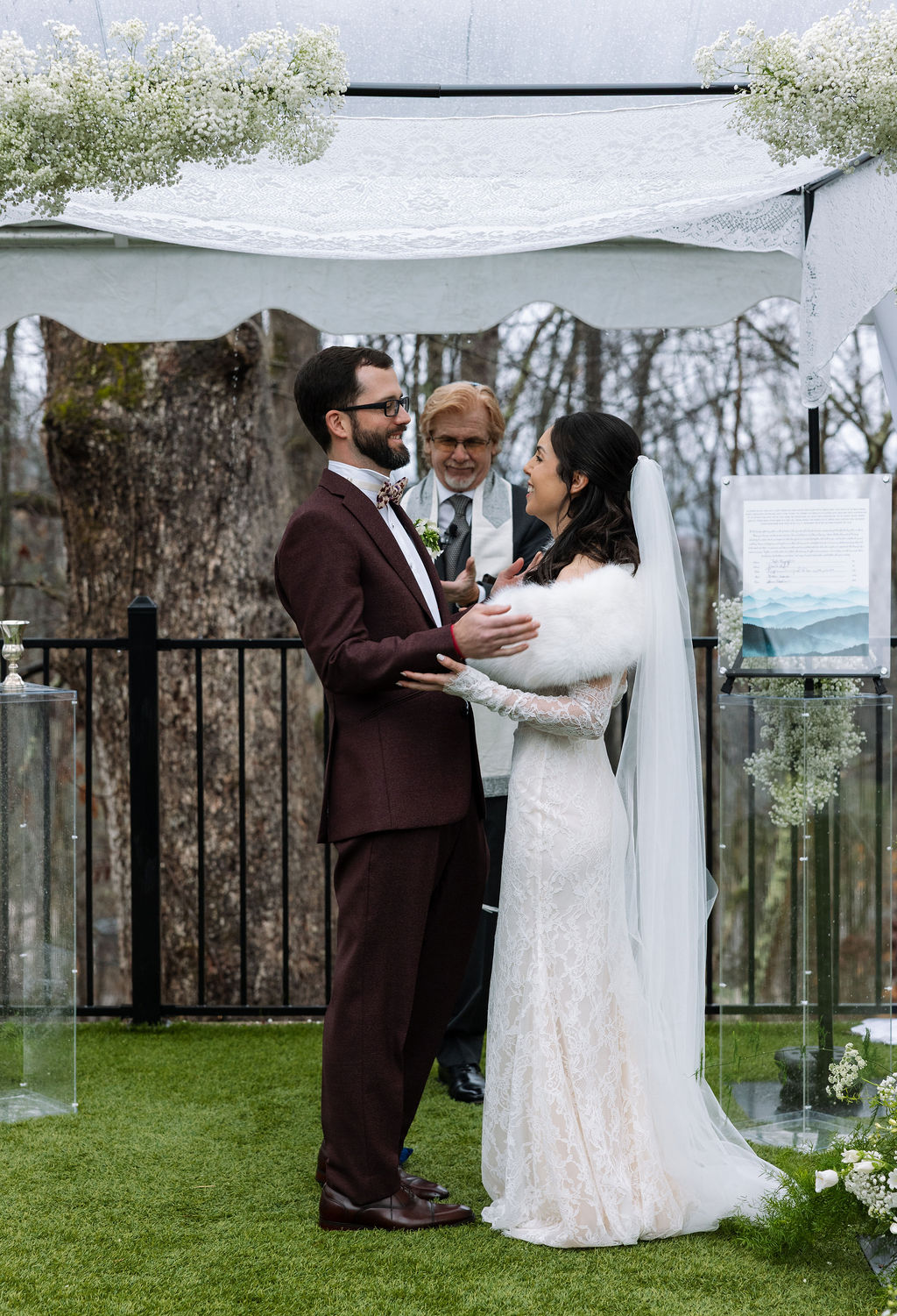 Bride and groom smiling at each other during their Tennessee wedding ceremony under a tent, rain softly visible beyond the covered space.