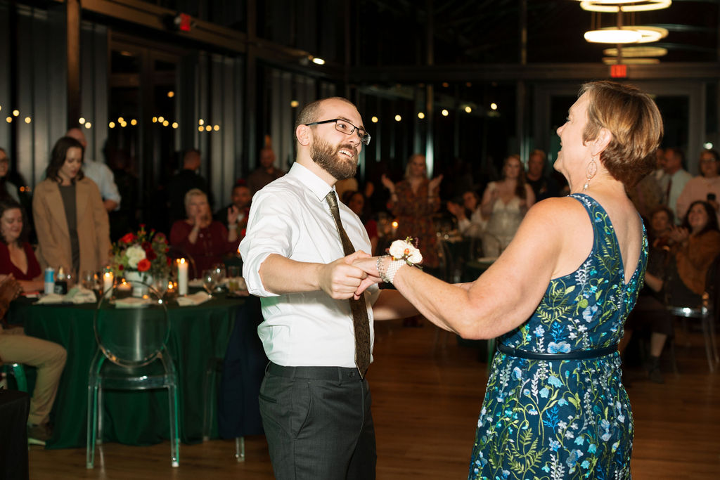 Mother and son dancing together during an intimate wedding reception, surrounded by seated guests and warm candlelight.