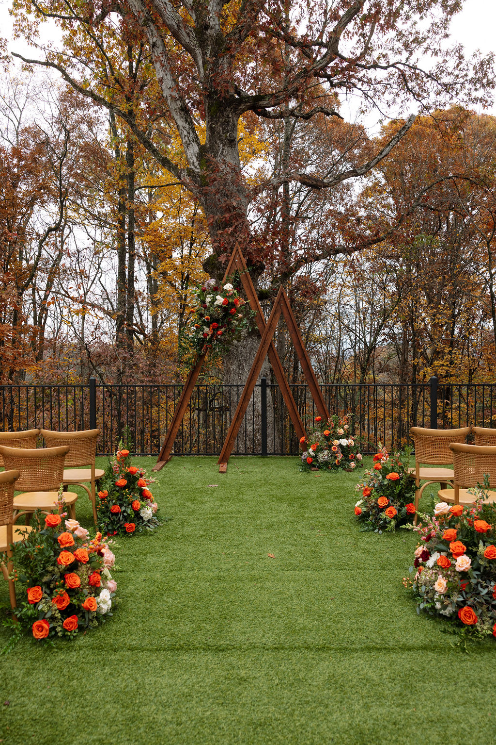 Wooden wedding arch in front of outdoor wedding ceremony set up with rustic chairs and warm florals throughout. 