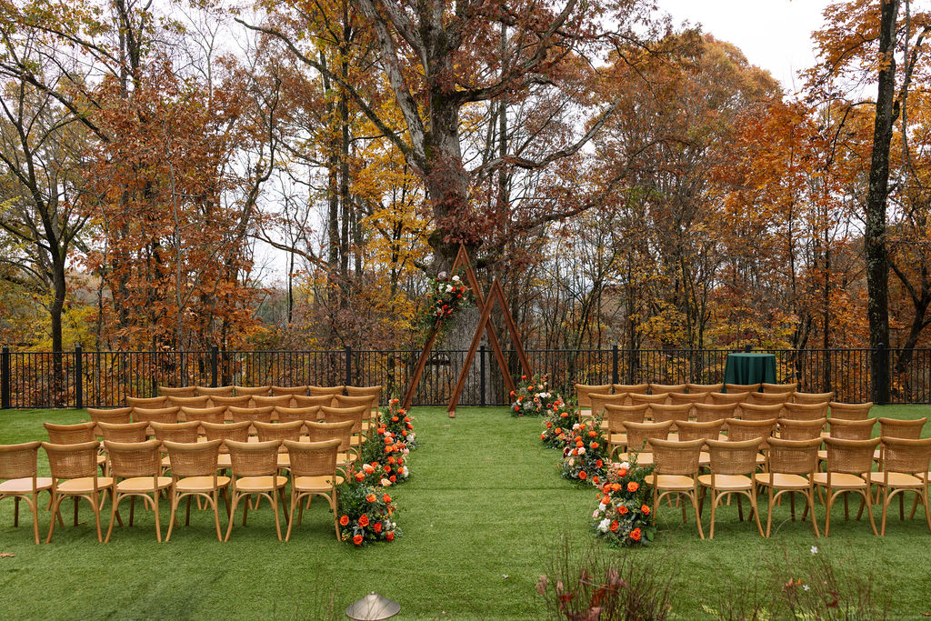 Outdoor ceremony setup at a Smoky Mountain wedding venue, with wooden chairs, fall florals, and trees surrounding the aisle.