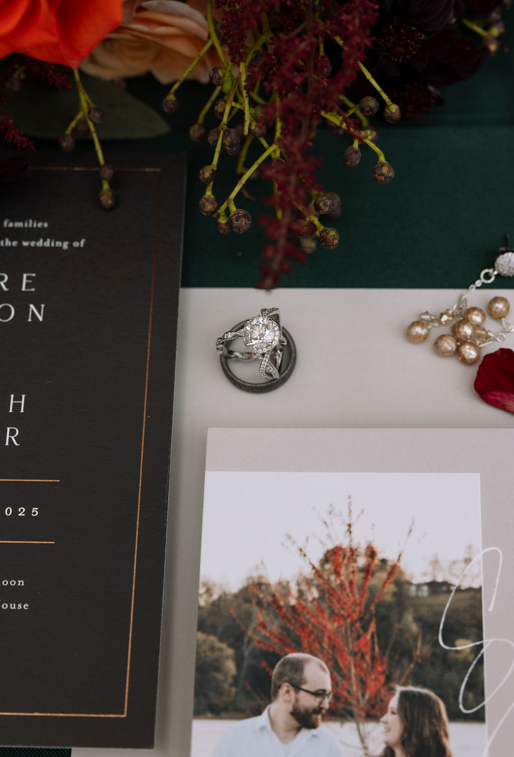 Wedding rings sitting on top of wedding details with wedding invitations and florals beside it.