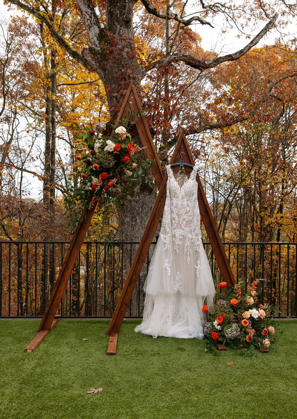 Lace wedding dress hanging on wedding arch with flowers outside beautiful Smoky Mountain wedding venue. 
