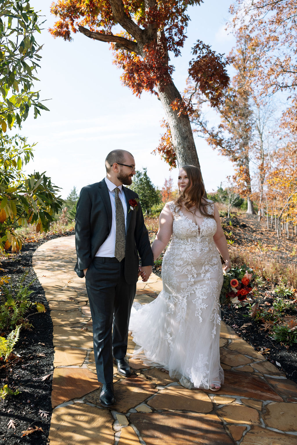 Bride and groom walking hand in hand along a garden path at a Smoky Mountain wedding venue during peak fall season.