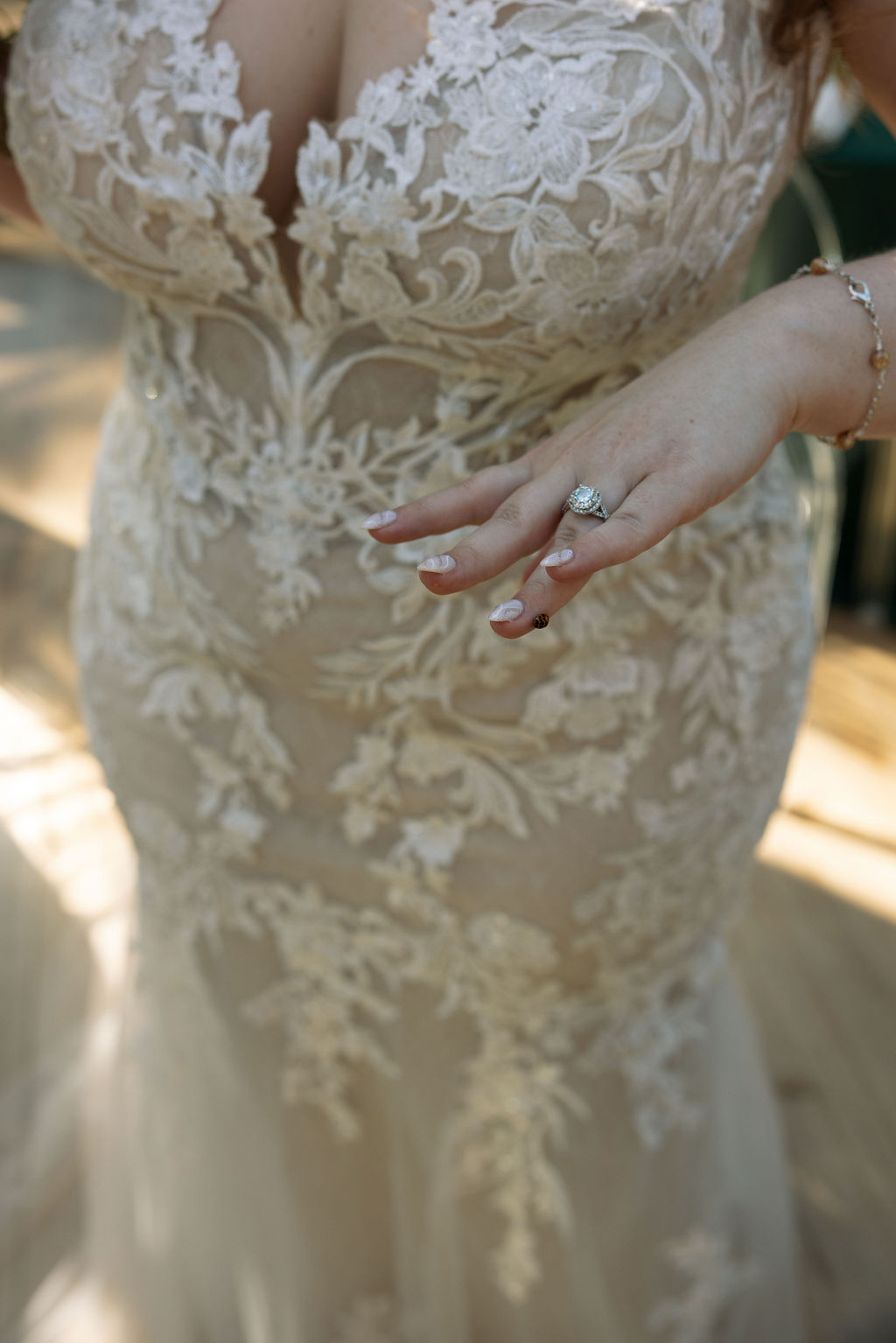 Bride wearing lace wedding gown and showing off engagement ring with ladybug landing on her finger. 