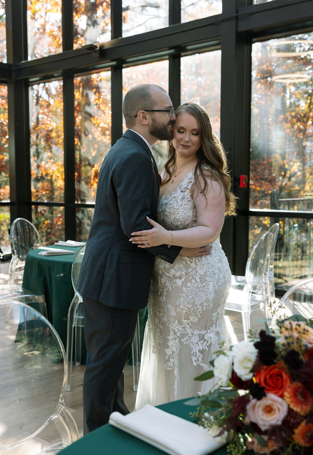 Bride and groom sharing a quiet moment inside a glass-walled reception space filled with natural fall light.