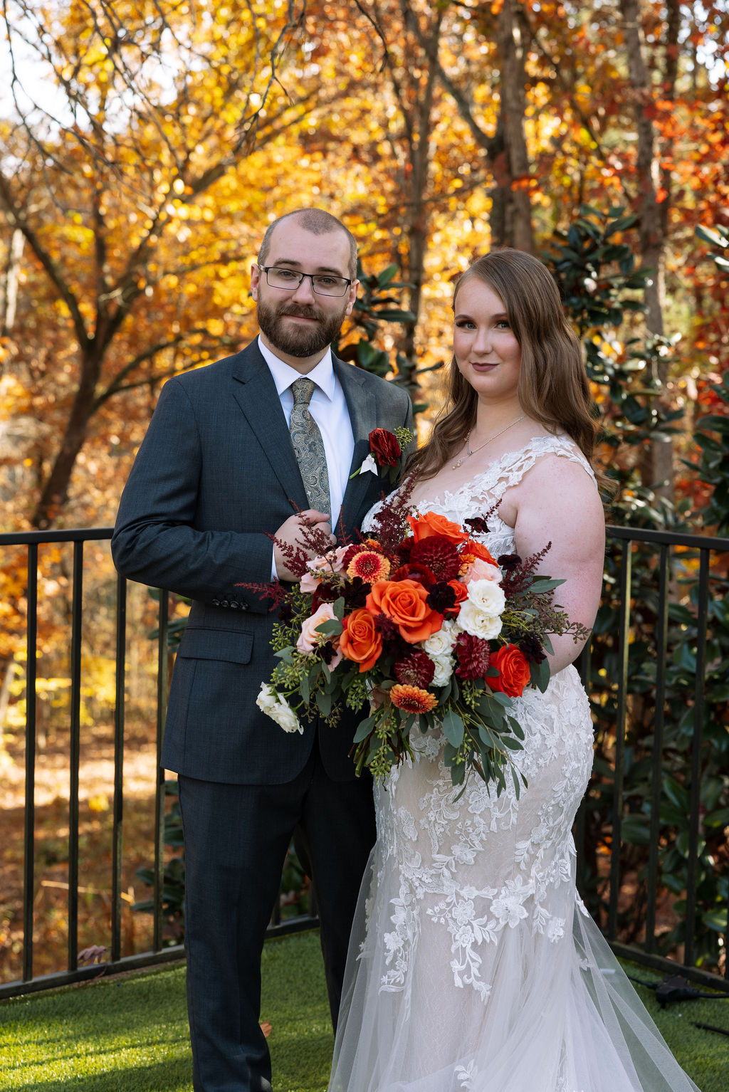 Wedding couple holding a vibrant fall bouquet at a Smoky Mountain wedding venue, with autumn trees in the background.