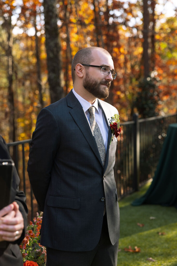 Groom standing quietly before the ceremony, surrounded by fall trees and soft afternoon light.