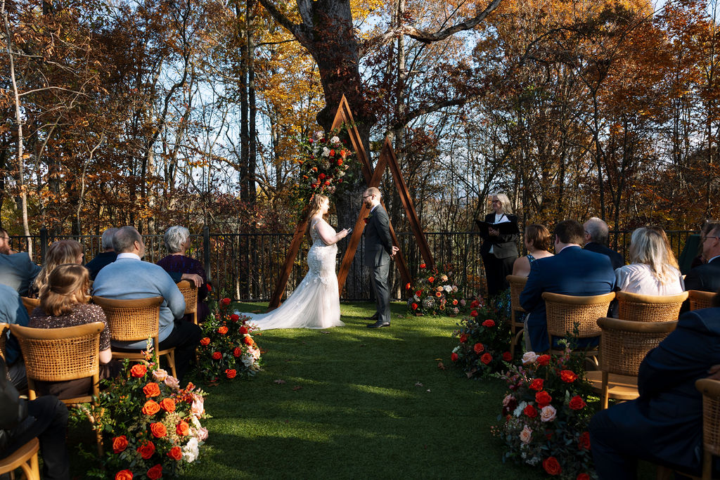 Outdoor wedding ceremony viewed from the aisle at a Smoky Mountain wedding venue, framed by autumn trees and floral arrangements.