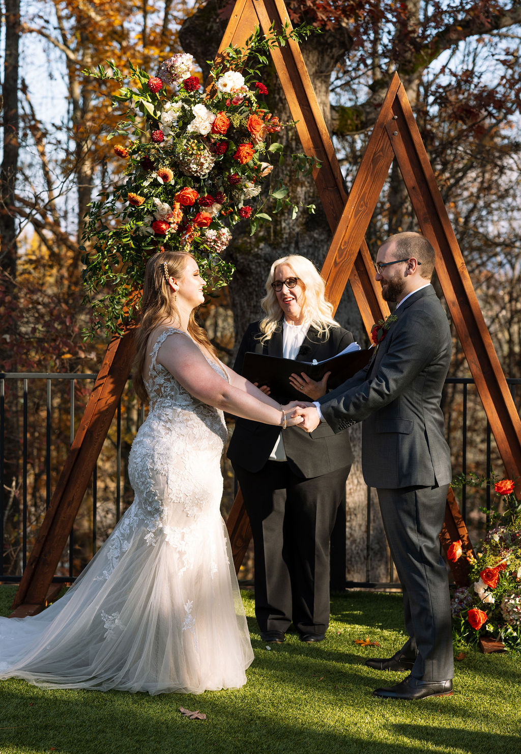 Bride and groom exchanging vows during an outdoor ceremony at a Smoky Mountain wedding venue, surrounded by fall florals and guests.