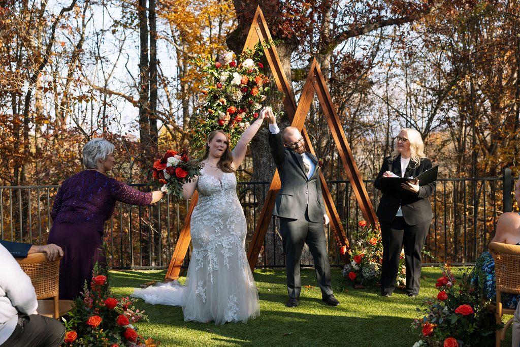 Newly married couple celebrating their ceremony recessional at a Smoky Mountain wedding venue, framed by fall florals and wooden arbor.