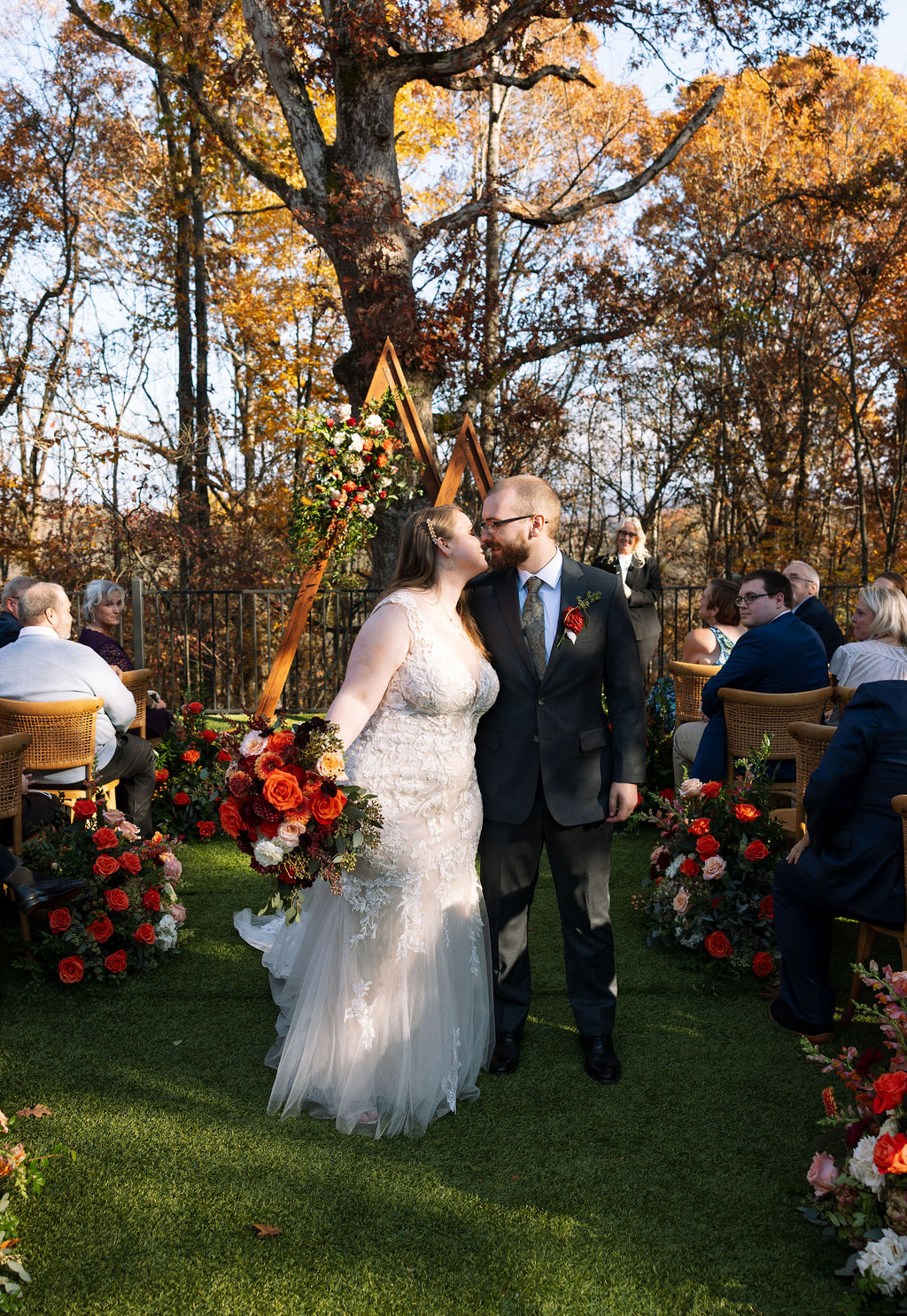 Bride and groom sharing a quiet kiss as they walk back down the aisle after their outdoor fall ceremony.