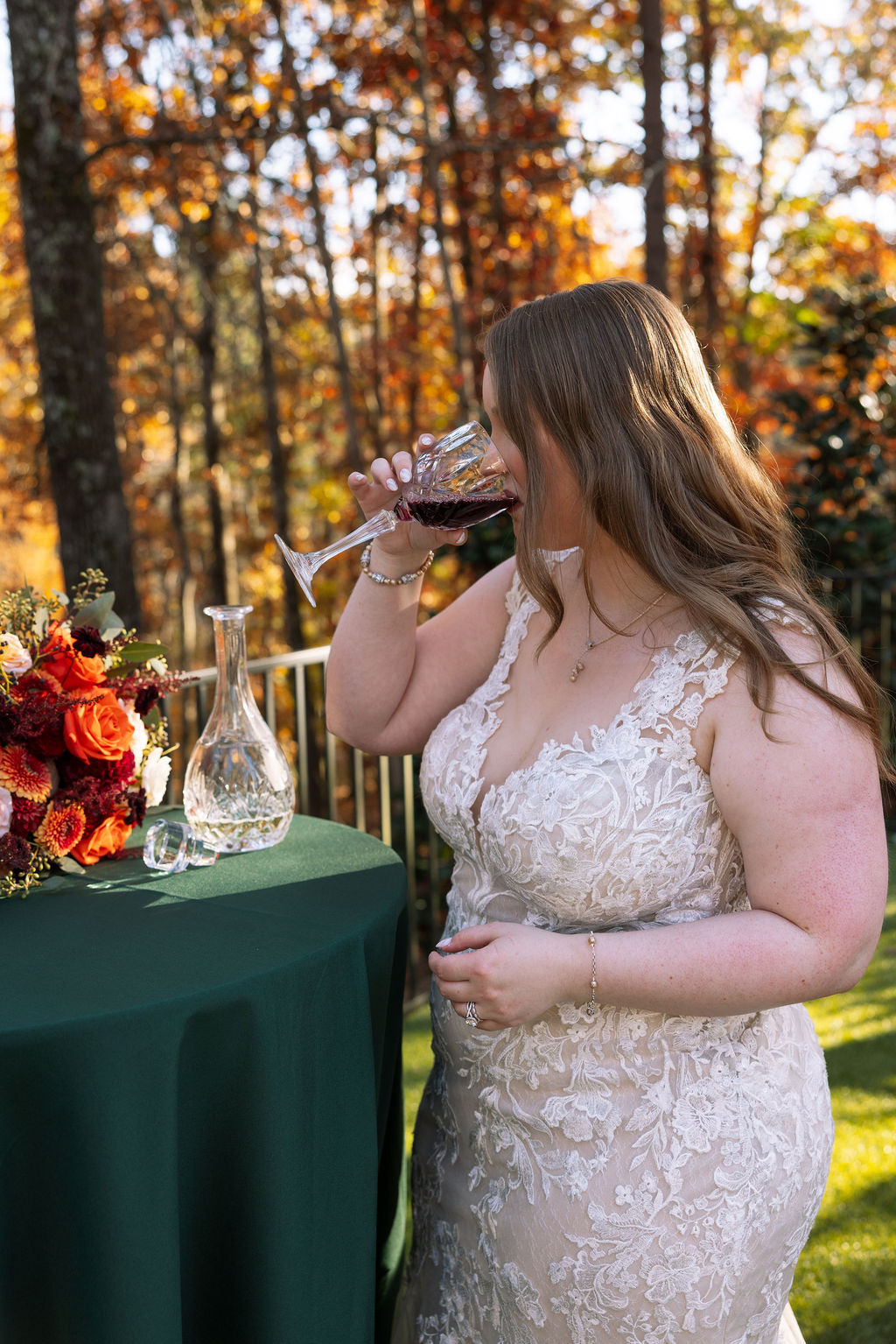 Bride taking a quiet moment with a glass of wine outdoors, surrounded by fall color and soft afternoon light.