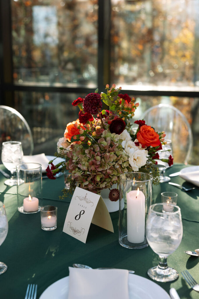 Wedding reception table with fall floral centerpiece, candlelight, and place settings inside a light-filled venue.