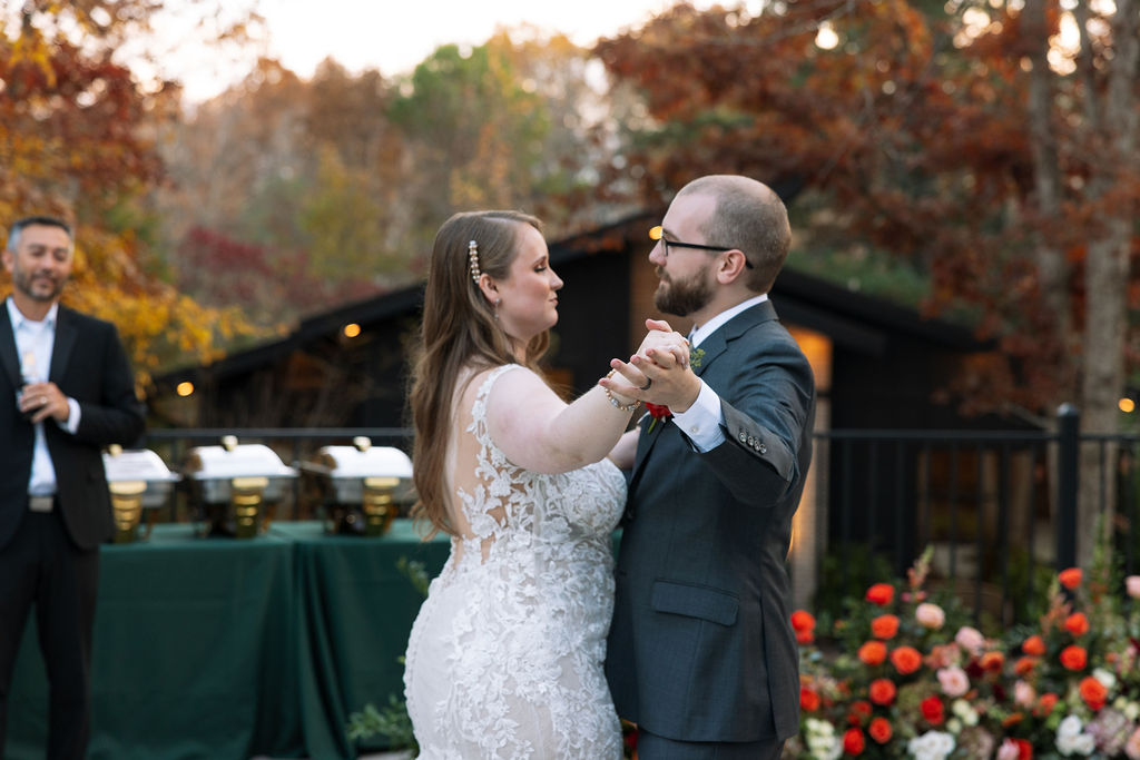 Bride and groom dancing together outdoors at a Smoky Mountain wedding venue, with fall florals and reception tables nearby.