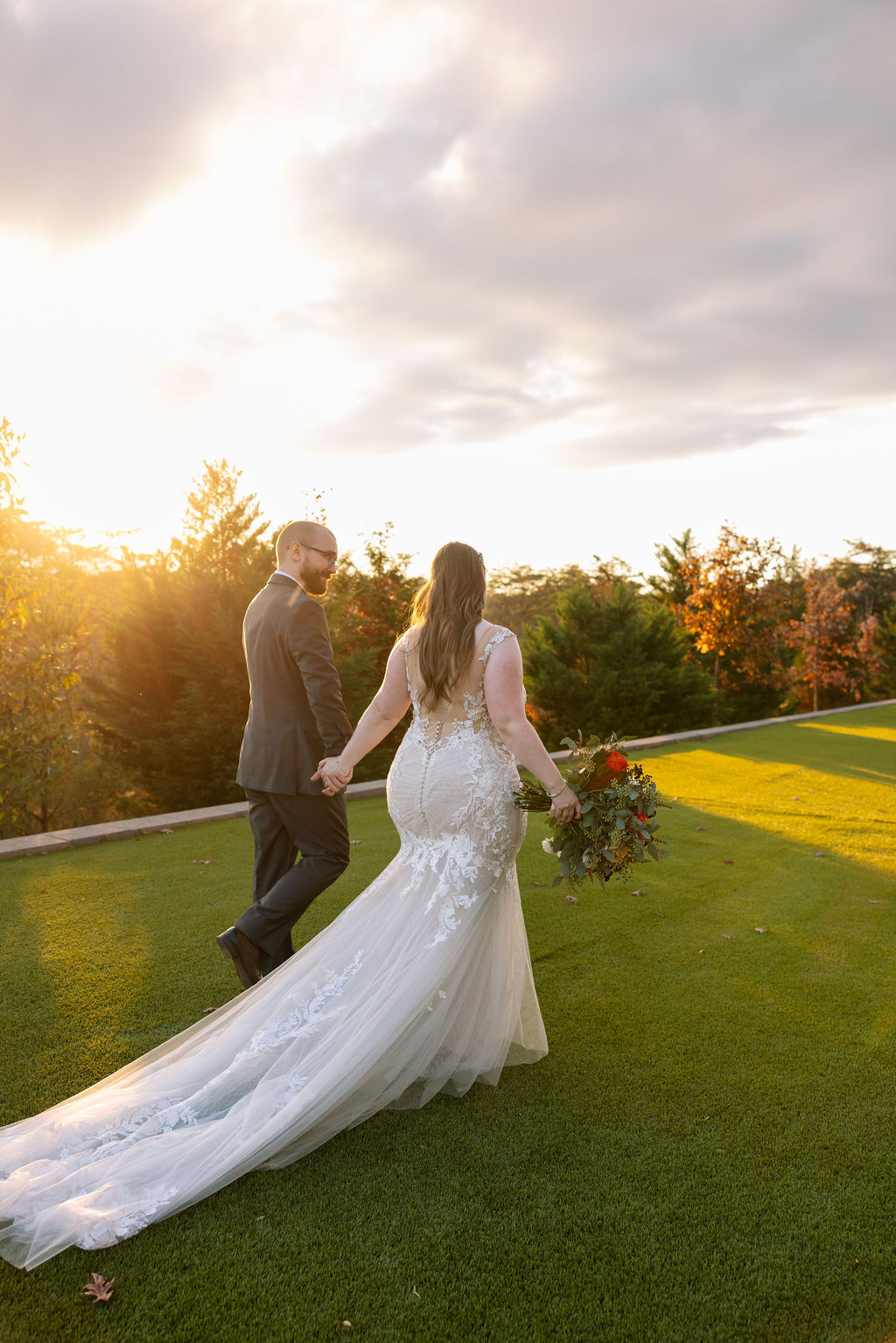Newly married couple walking hand in hand across grassy area during golden hour celebrating recent marriage. 
