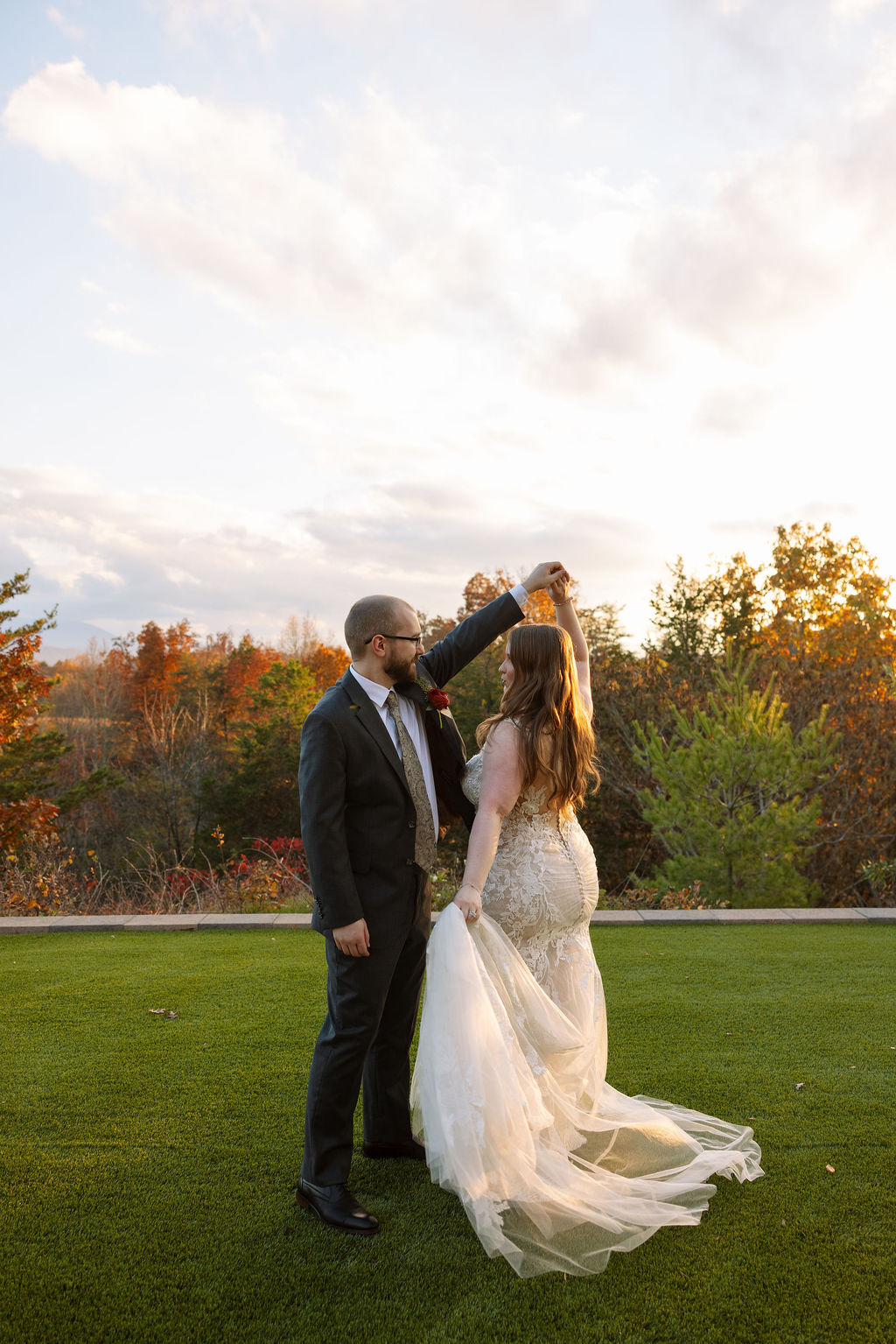 Bride and groom twirling together during golden hour, with fall trees and open sky creating a relaxed, romantic moment.