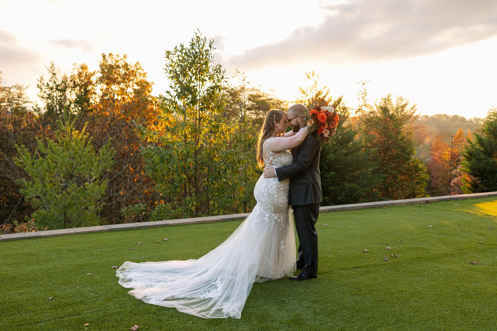 Bride and groom embracing during golden hour at a Smoky Mountain wedding venue, with autumn trees glowing behind them.