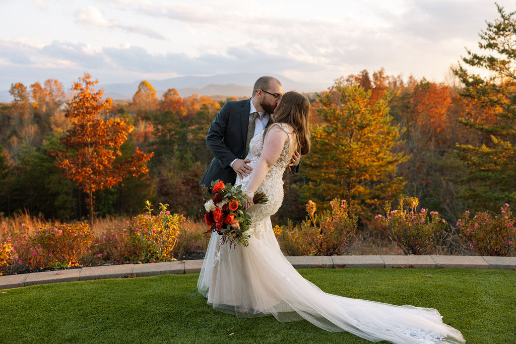 Bride and groom kissing at a Smoky Mountain wedding venue, framed by vibrant fall foliage and distant mountain views.