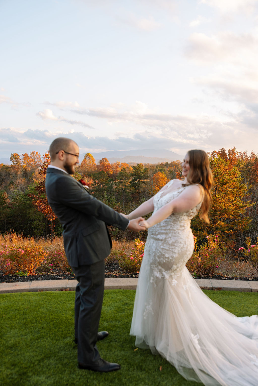 Bride and groom laughing together while holding hands at a Smoky Mountain wedding venue, with fall foliage and mountains in the distance.