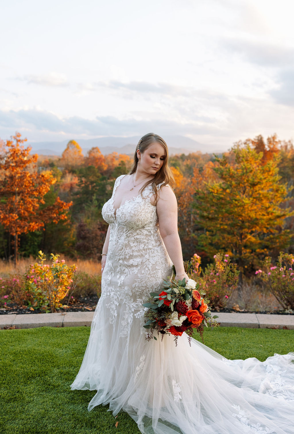 Bride standing outdoors at a Smoky Mountain wedding venue, holding a fall bouquet with colorful foliage and mountain views behind her.