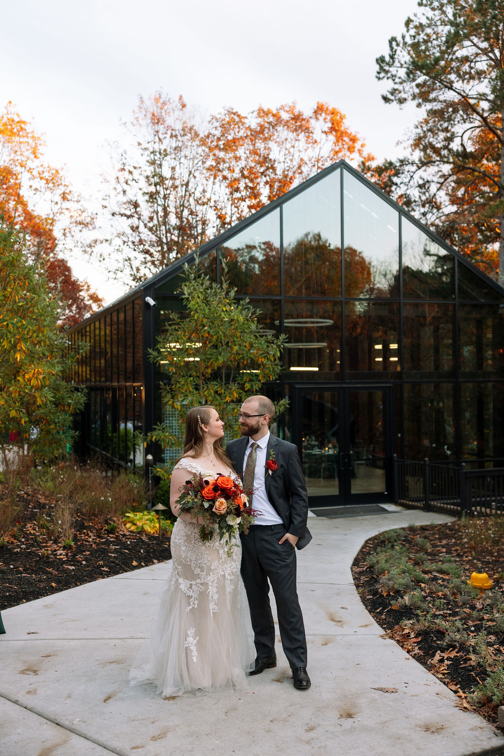 Bride and groom standing together outside a modern Smoky Mountain wedding venue, framed by glass architecture and autumn trees.