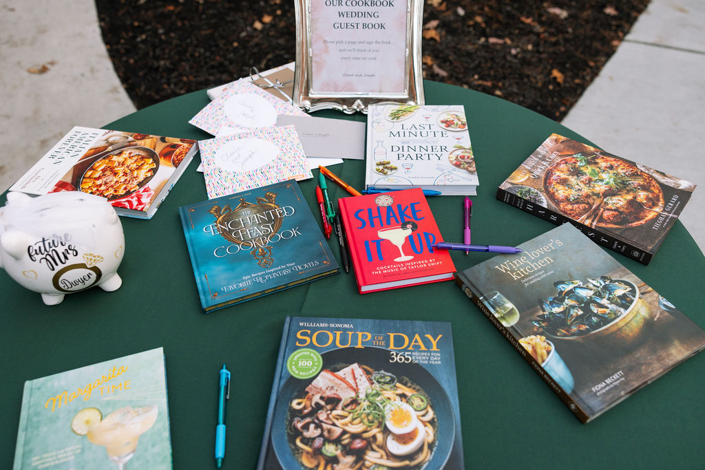 Creative wedding guest book table featuring cookbooks, handwritten notes, and personal details for guests to sign.