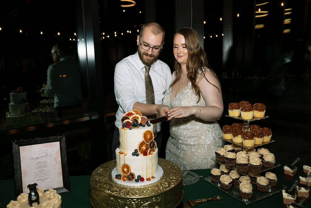 Bride and groom cutting their wedding cake inside a Smoky Mountain wedding venue, surrounded by a curated dessert display.